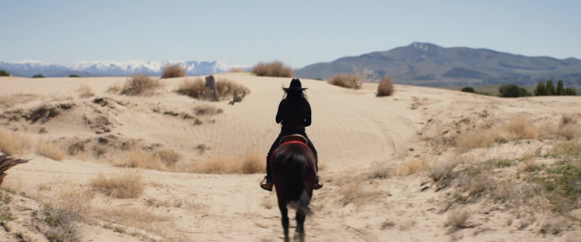 A woman rides a horse across a desert