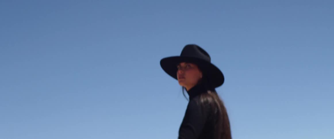 Woman wearing a black wide hat rides a black horse