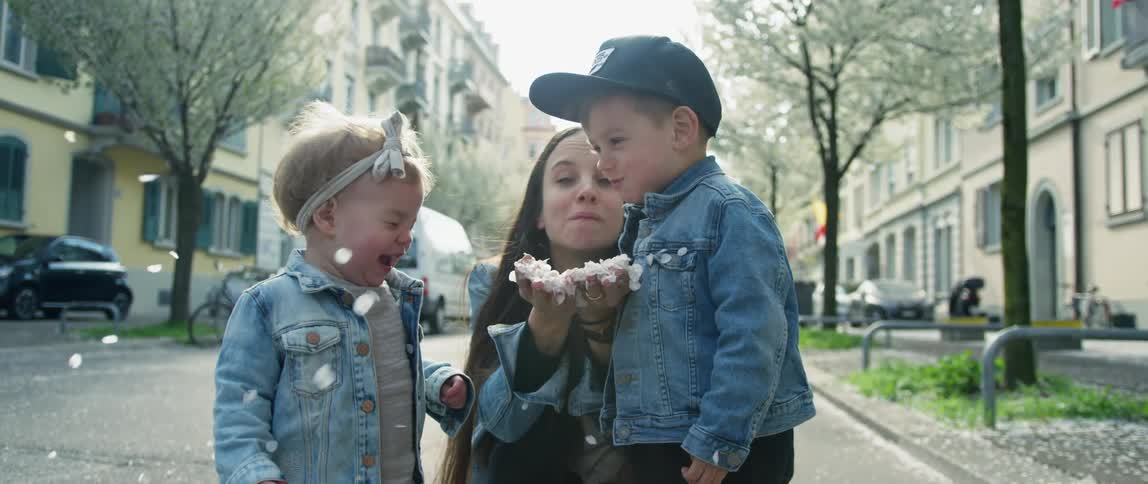 Mother plays with her children blowing flower petals on the streets