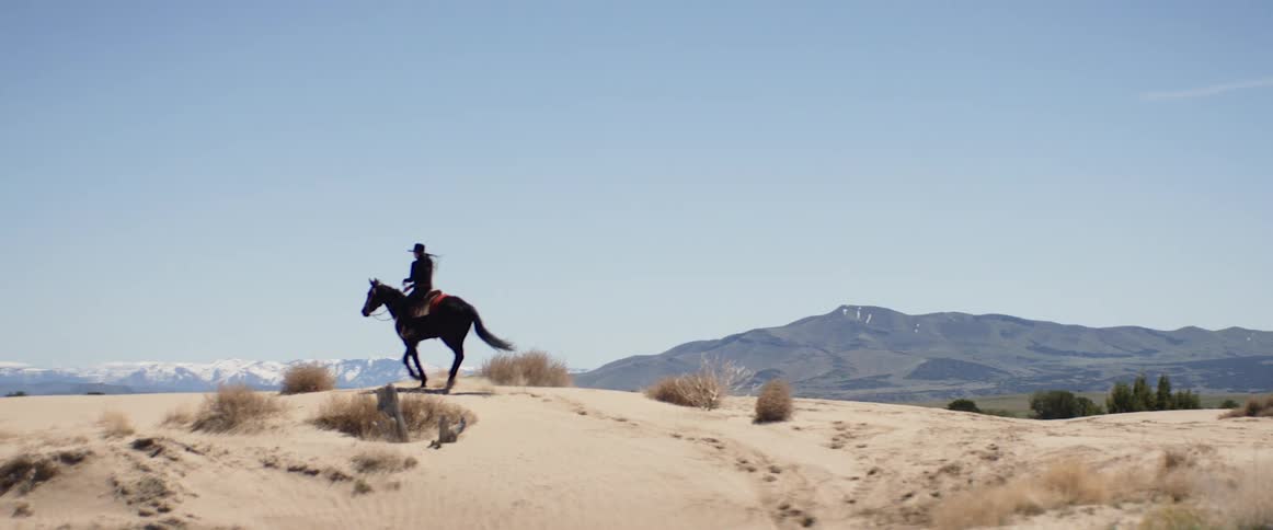 Woman rides a dark horse uphill in the desert