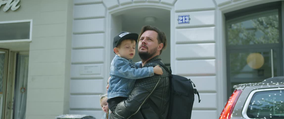 A man carrying a small boy and a young woman carrying a baby girl walking down a city street