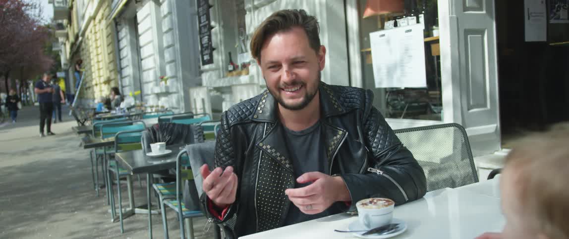 A man sits with other people at a table at a cafe