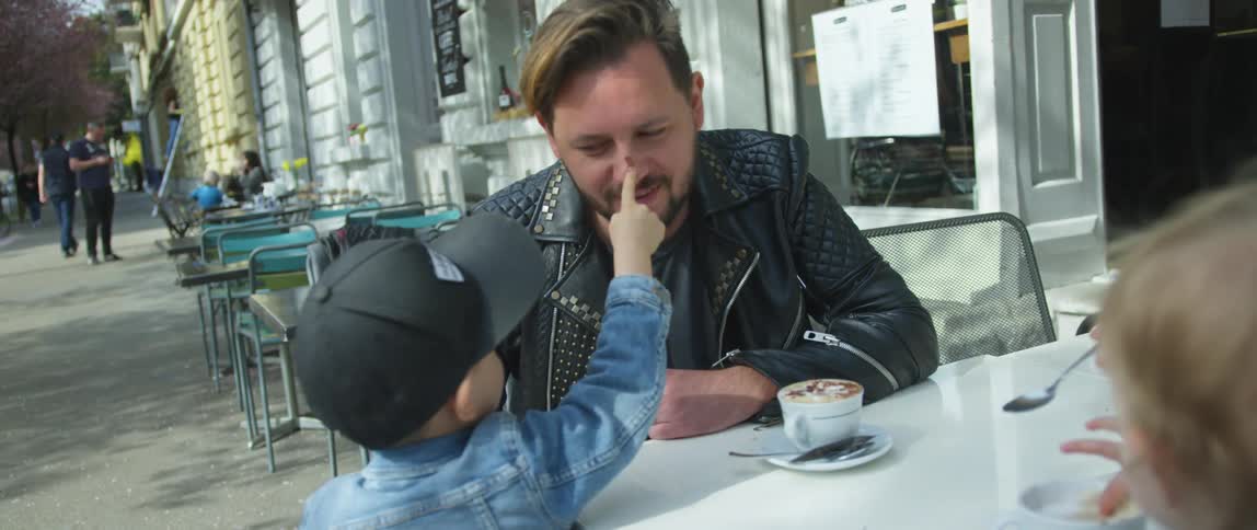 Boy playfully touches father nose while sitting on a street caf