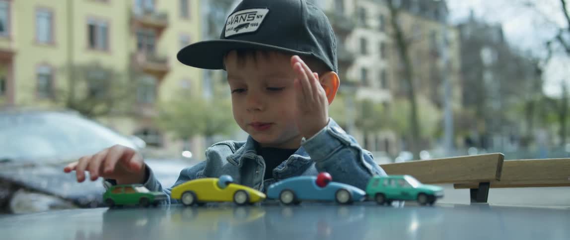 A boy sitting at a table lining up a group of toy cars