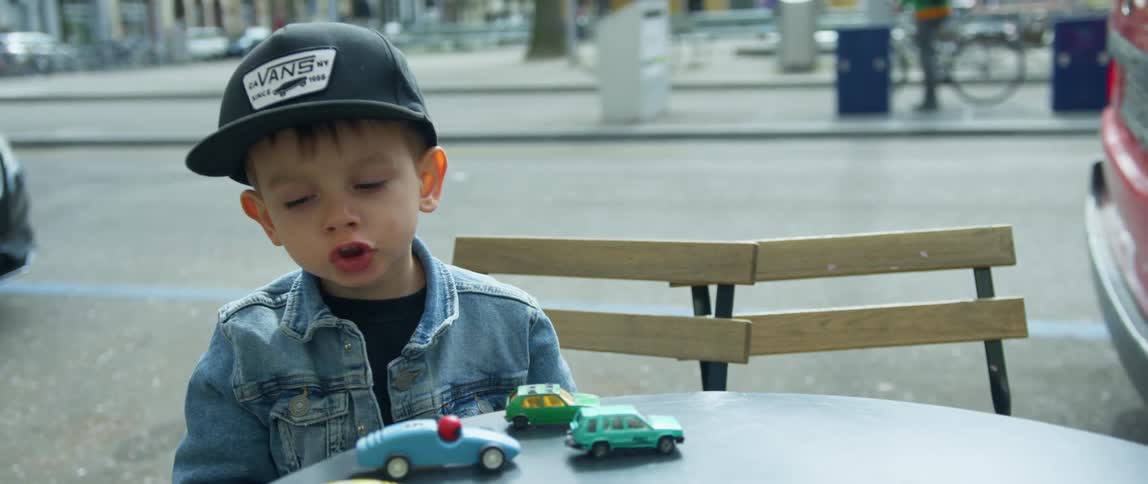 A young boy sits at an outdoor table and plays with toy trucks