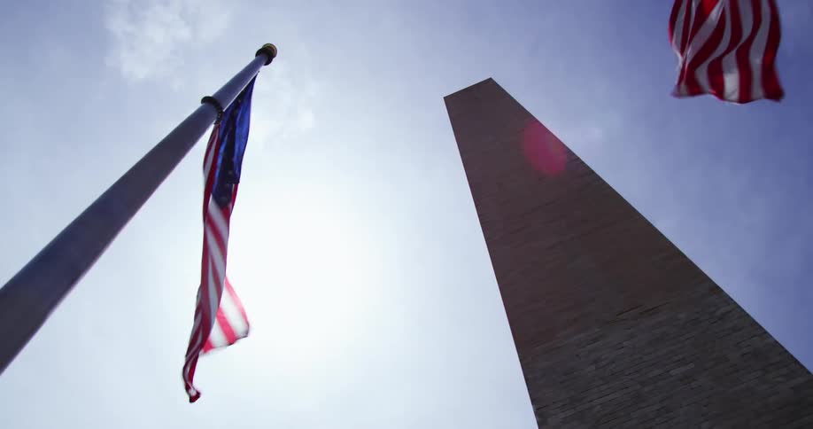 American flags on poles wave in the wind in front of the monument