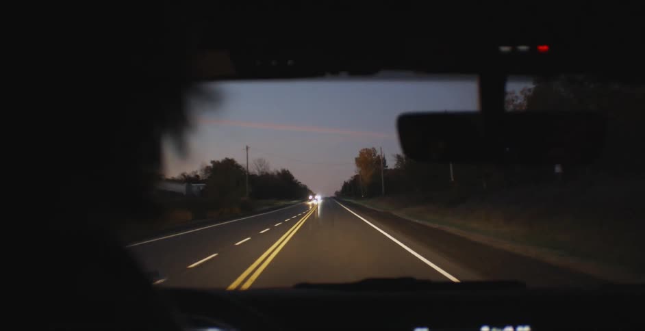 A person drives a car down a road at dusk