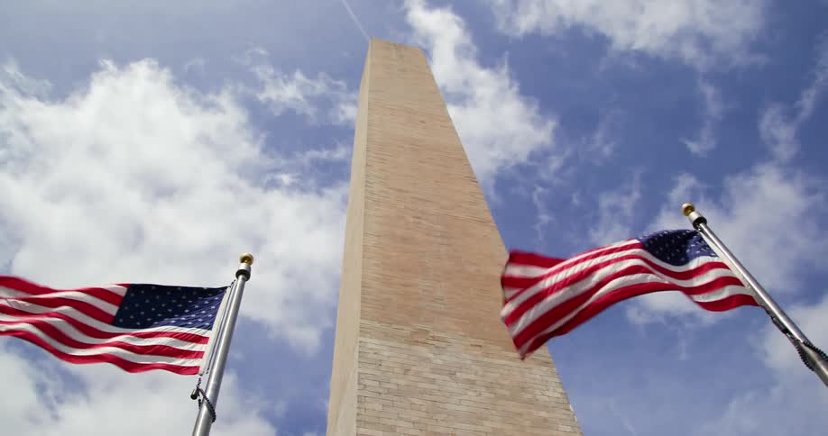 Two american flags fly in the breeze in front of the washington monument
