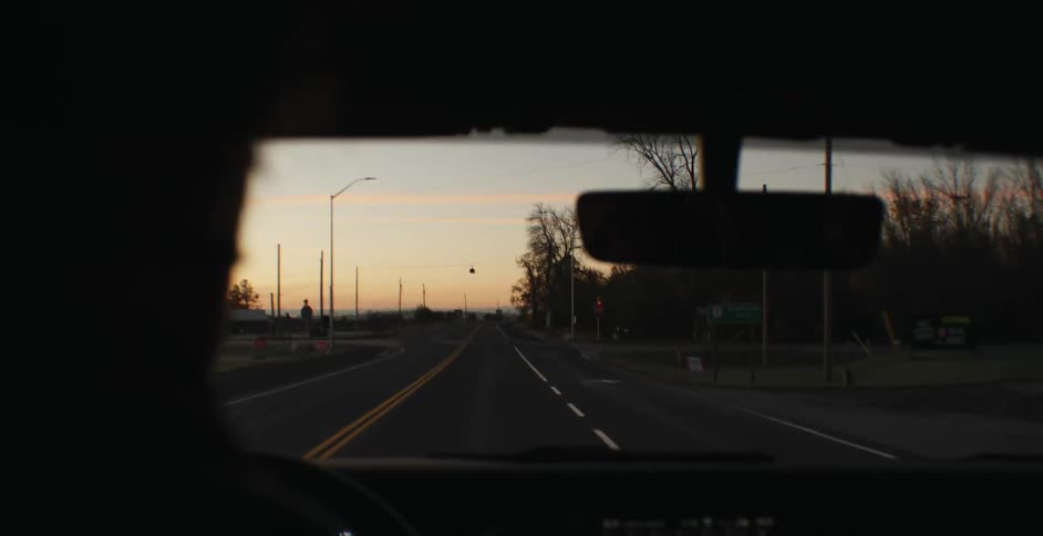 A person driving a vehicle down a well kept road at sunset