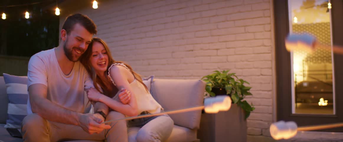 A woman cuddles up to a man as him and others roast marshmallows outside a home