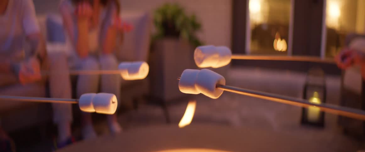 Several people roast marshmallows on a long stick over a fire