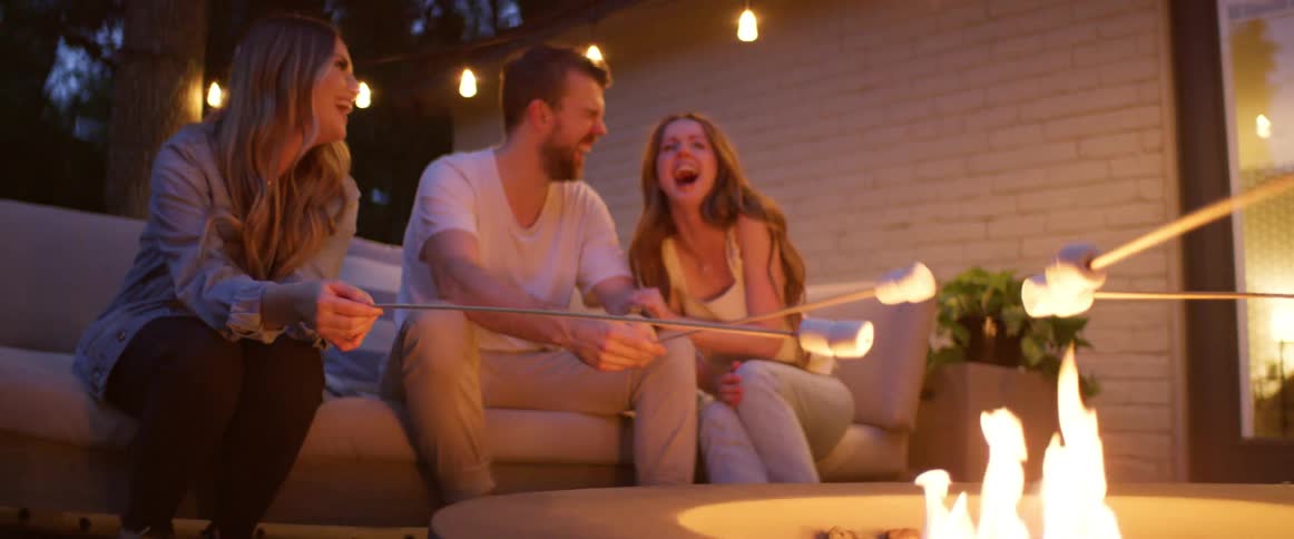 Friends sit outdoors roasting marshmallows over fire pit