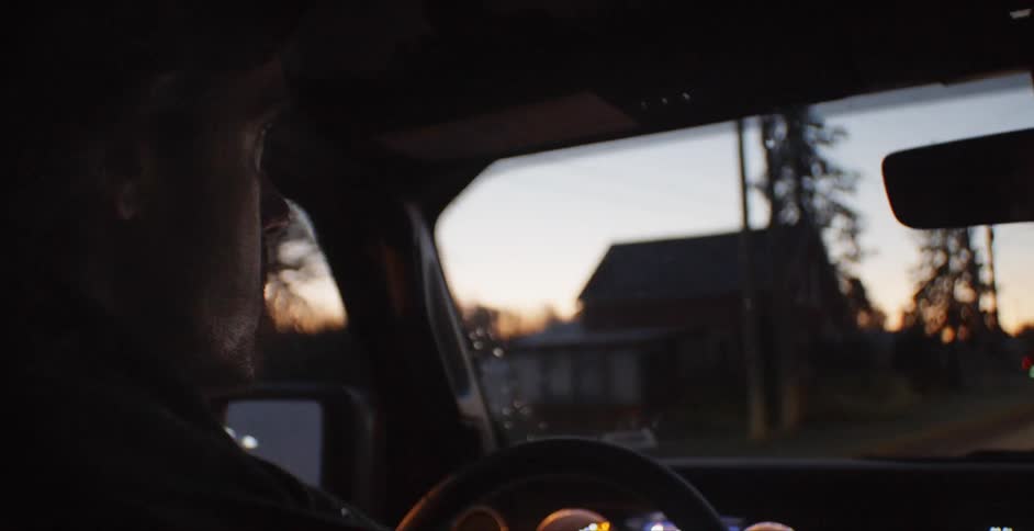 A man drives through a tree lined neighborhood at dusk