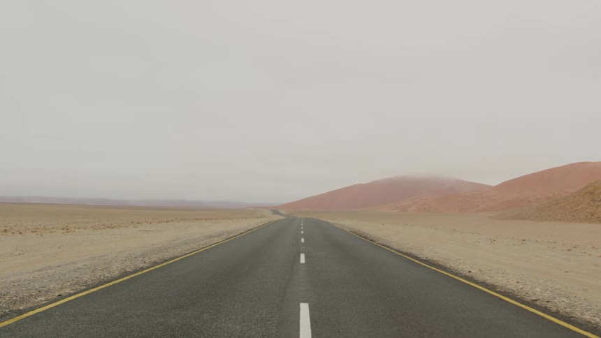 A road through a hilly grassland with yellow and reddish grass under a cloudy sky