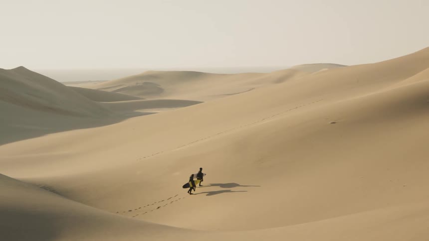 Two men holding surfboards walk in the desert