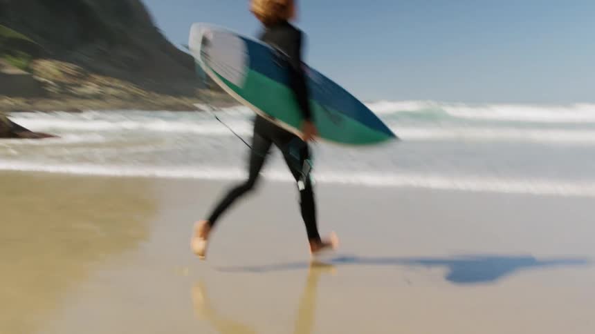 Surfer holding a surfboard runs to the wavy ocean
