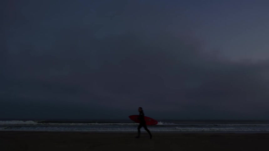 A person is running on the beach while holding a surfboard