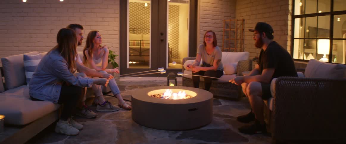 A group of friends sit outside a house and roast marshmallows