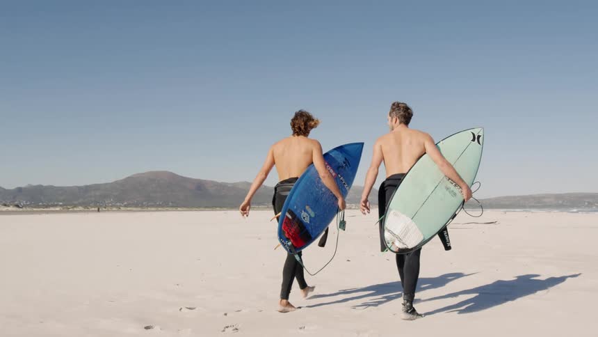Surfers walk on the white sand beach next to the sea