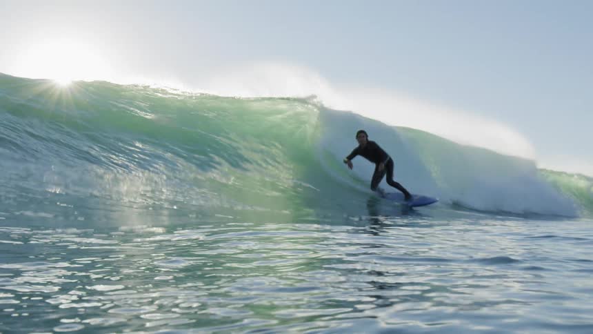 Surfer in wet suit rides wave as large sun glares down