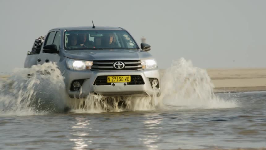A truck drives through a shallow stream in the desert