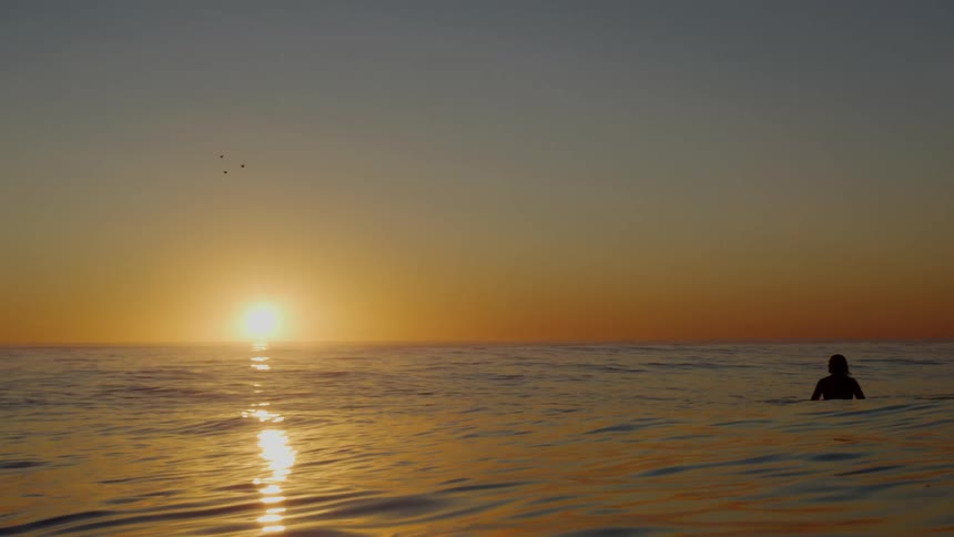People are swimming in the ocean while the sun is setting