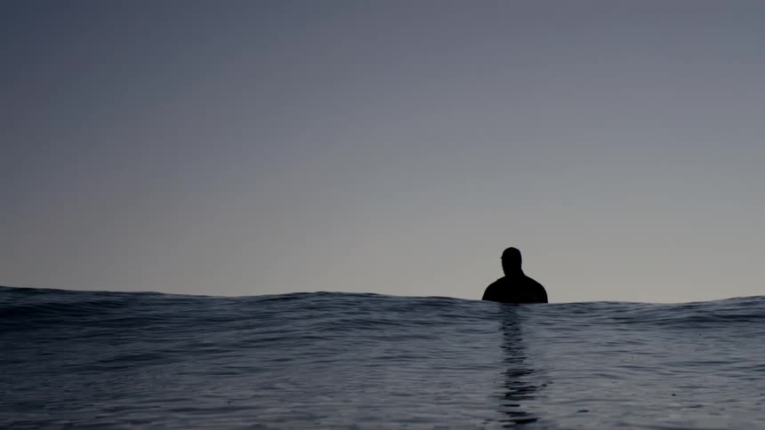 A large wave rolls past a man standing in the ocean