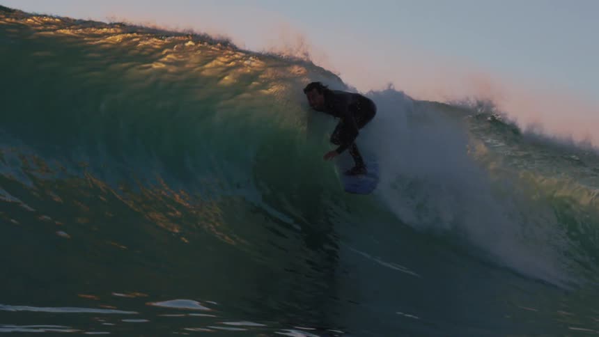 Surfer uses a surfboard to ride a wave in the ocean at sunset