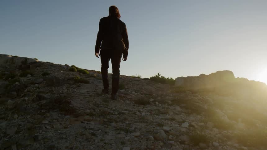 A white man walks up a rock covered hill