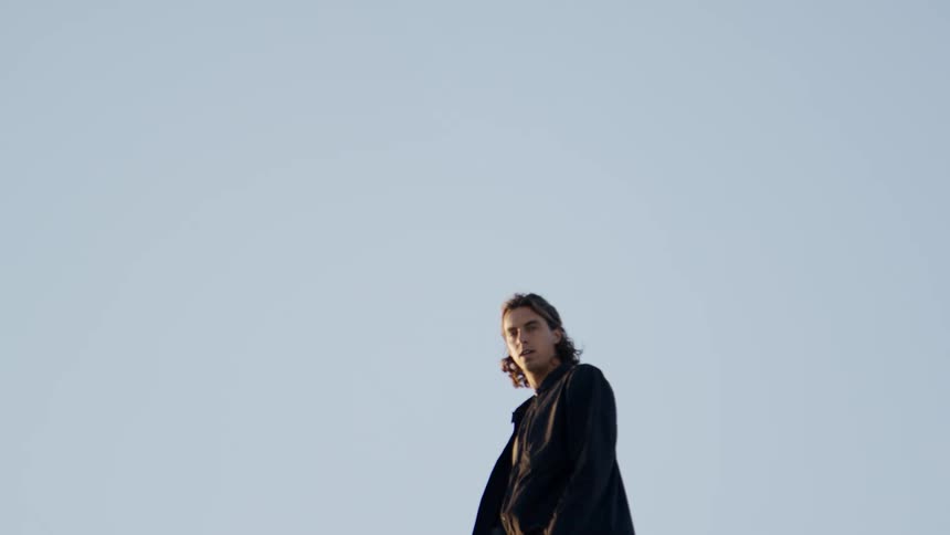 A white male clad in black walks along the top of a sand dune
