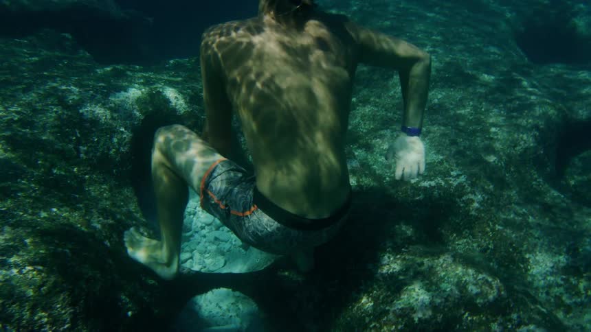 A man wearing a snorkel mask pushes off the rock at the bottom and swims to the surface