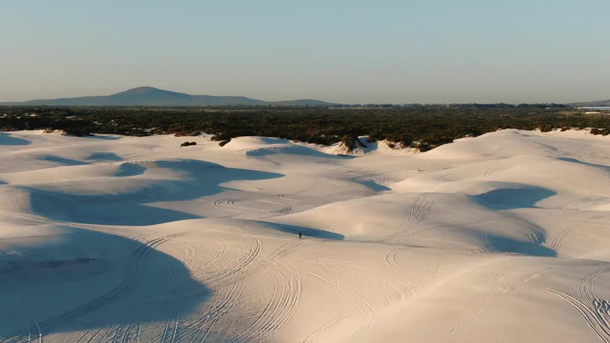 A person walks over the white sand dunes of a desert
