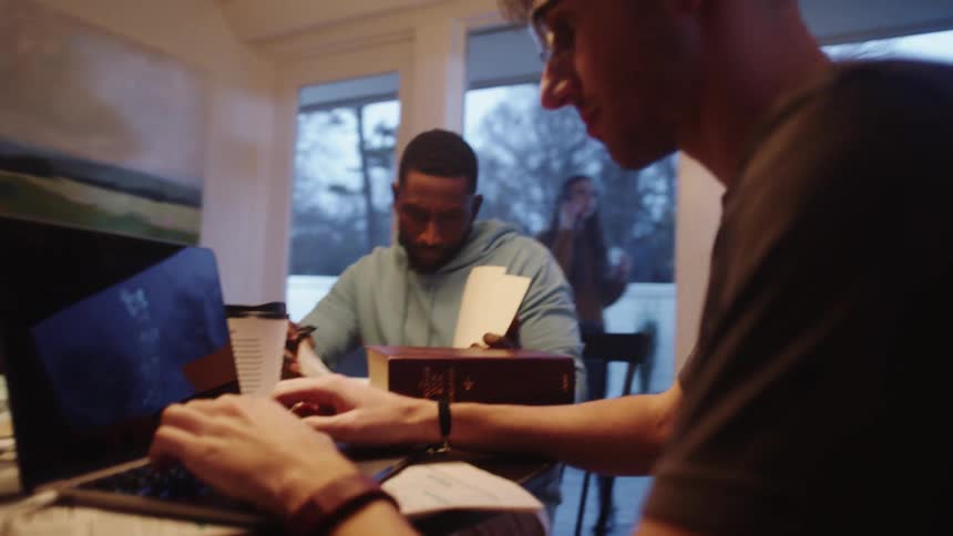 Three people in a home work on a computer shuffle papers and talk on a phone