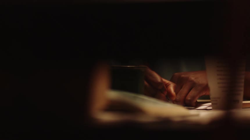 A person spies through a window on a woman sitting at a desk and writing