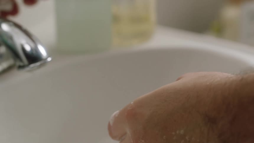 A white man puts soap on his hands and washes them in a sink