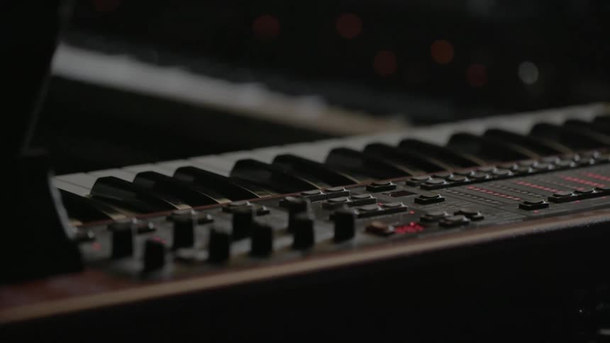 An electronic keyboard with lights flickering and another keyboard in the background
