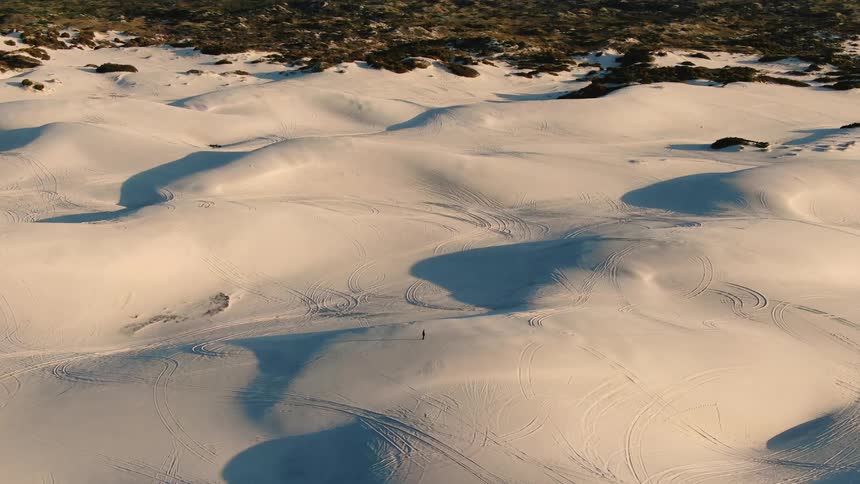 A person walks over a sand dune in a desert