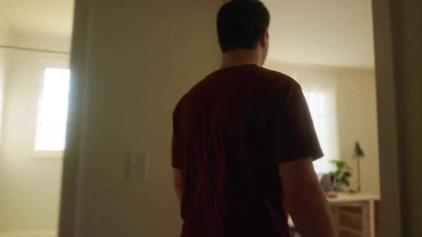 A white man walks through a house and into a room with a table and a chair