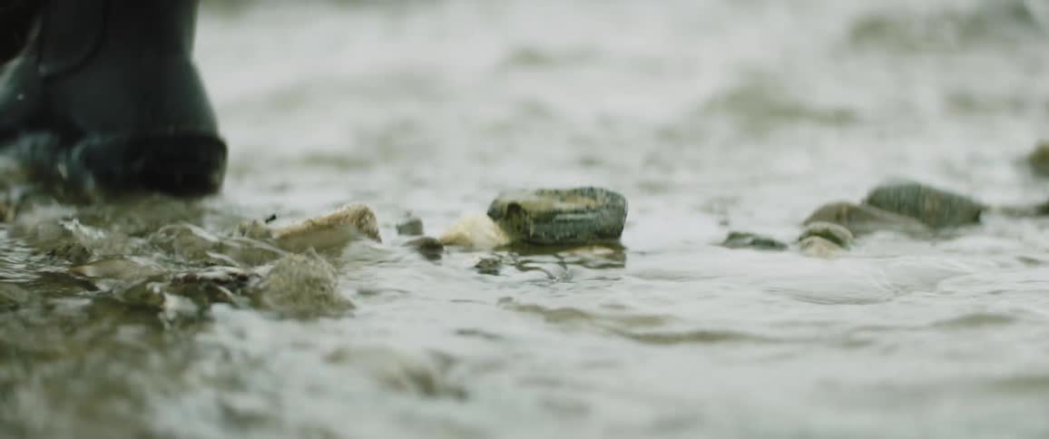 A person wearing boots steps across a shallow stream