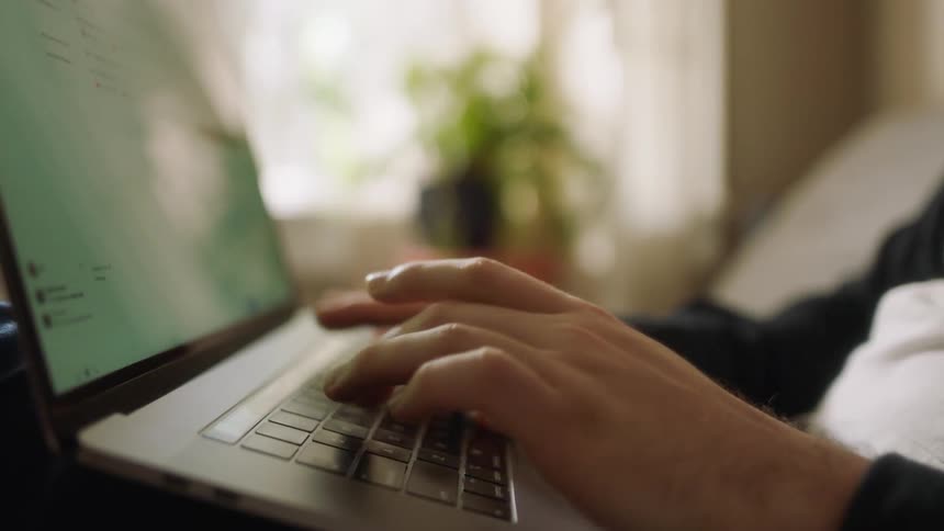 A man sits in a room typing on a laptop
