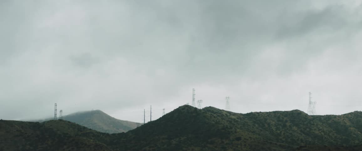Dark clouds hover over mountains with transmission towers on them