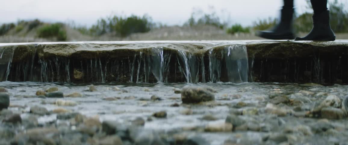 Person wearing rain bootssplashes through water flowing into pebble littered stream