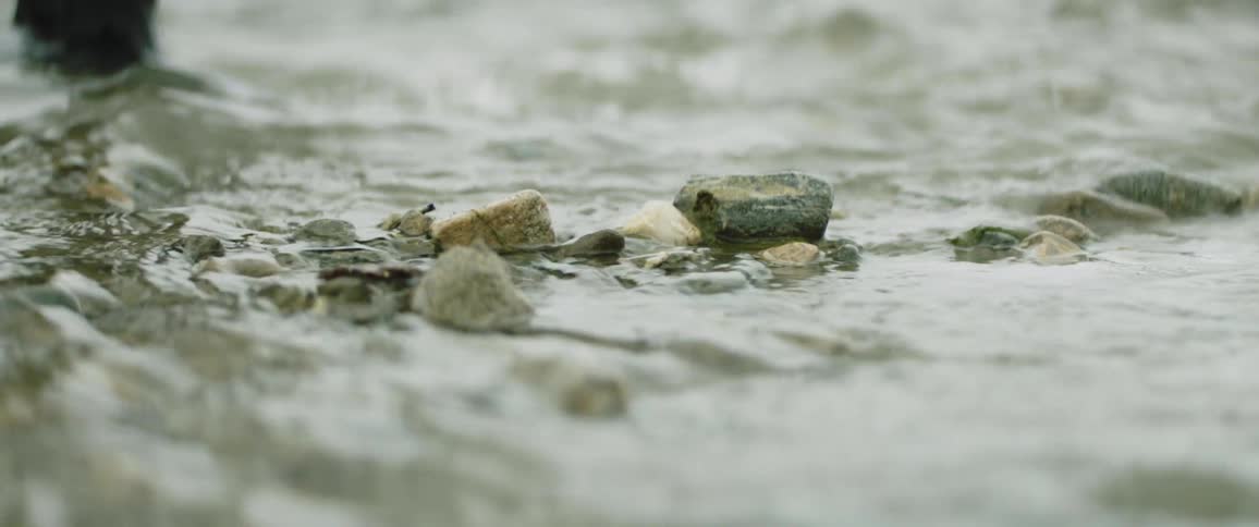 A person in rain boots walks through streaming water