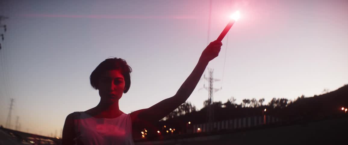 A woman holds up a burning flare at dusk