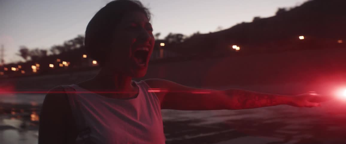 A teenager stands outside and holds her arm out while holding a flare and yelling