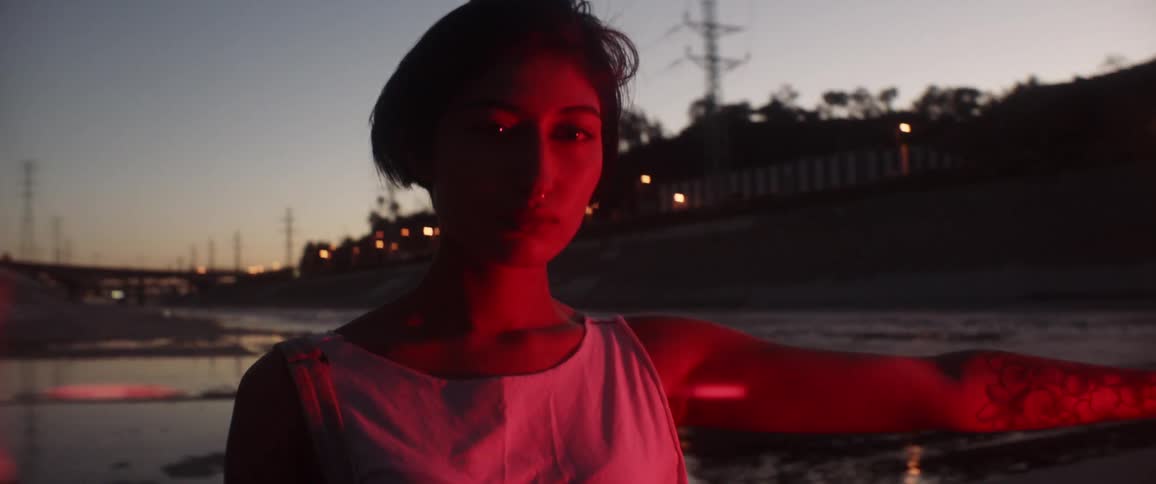 A hispanic woman stands near the los angeles river and holds a lit road flare