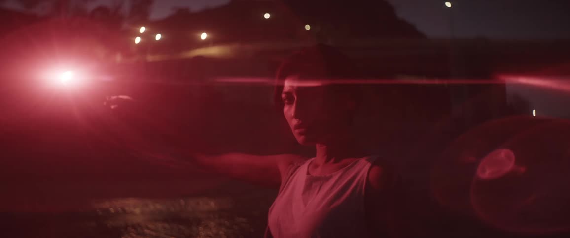 Woman holding a red emergency flare stands near a river at night