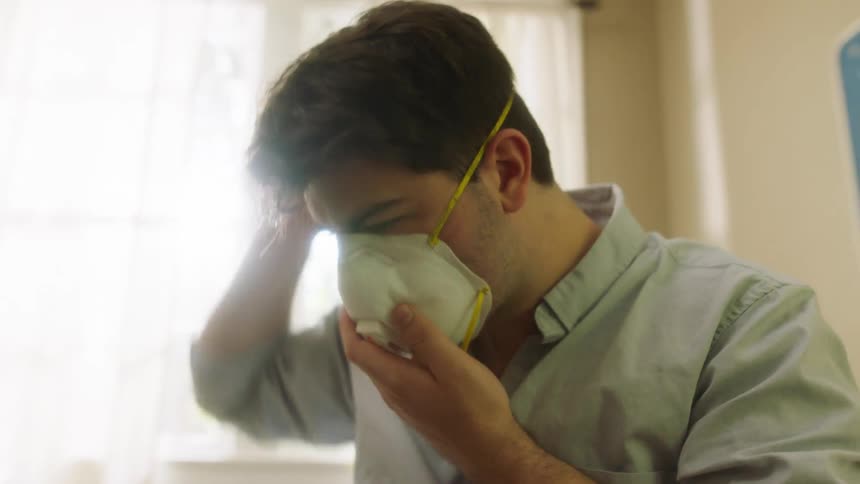 Man sitting in bed puts face mask on before going out