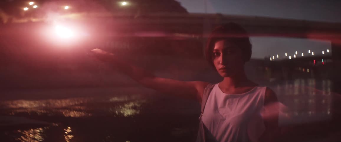 A woman holds a lit flare and lowers it to her side