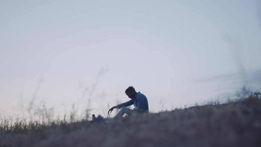 A man sitting on a grassy field with the sky in the background